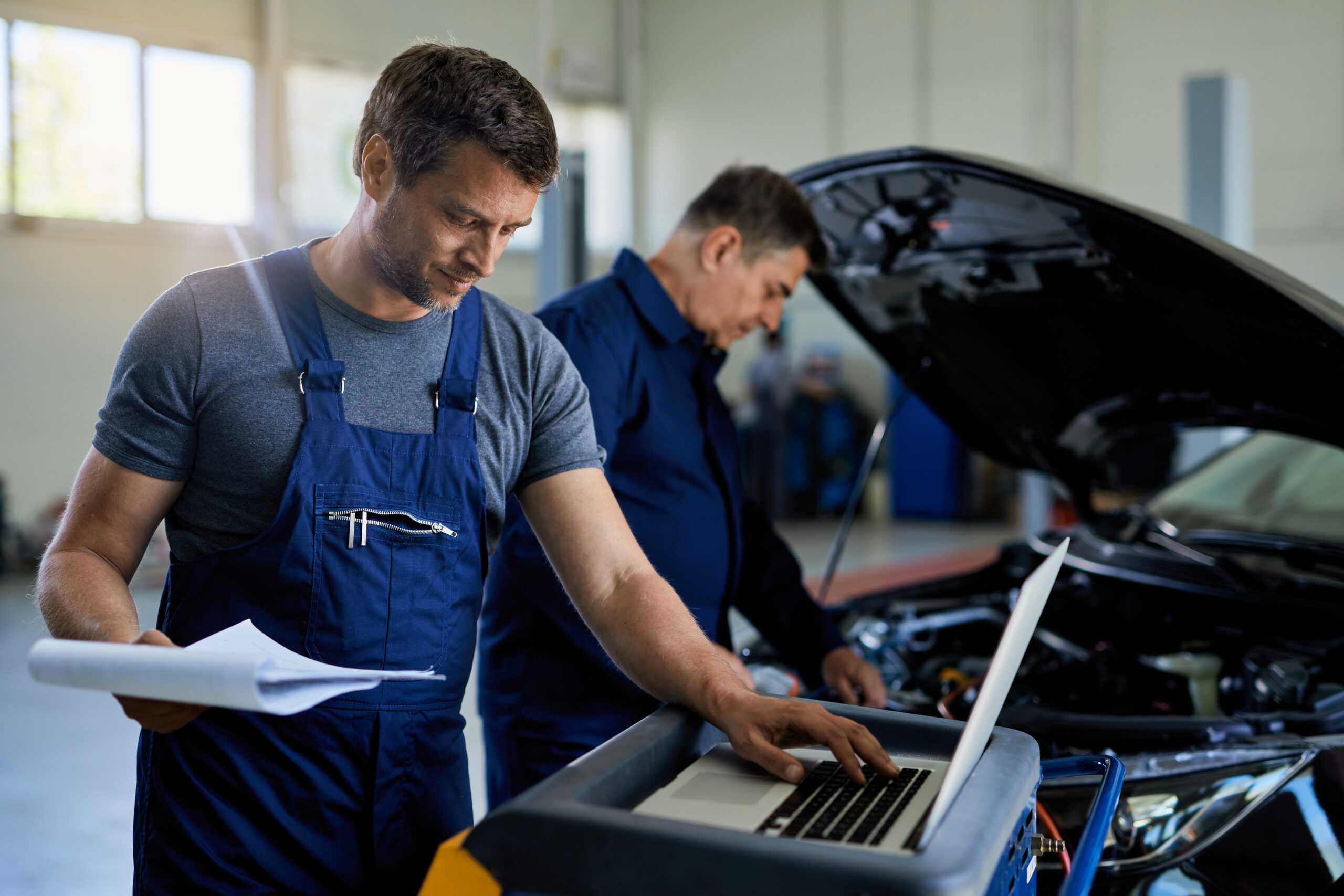 meccanico effettua una diagnosi ad un automobile utilizzando un laptop