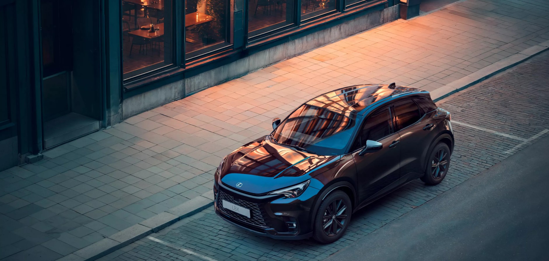 Lexus LBX Vibrant Edition nera in contesto urbano al tramonto, ripresa dall’alto.