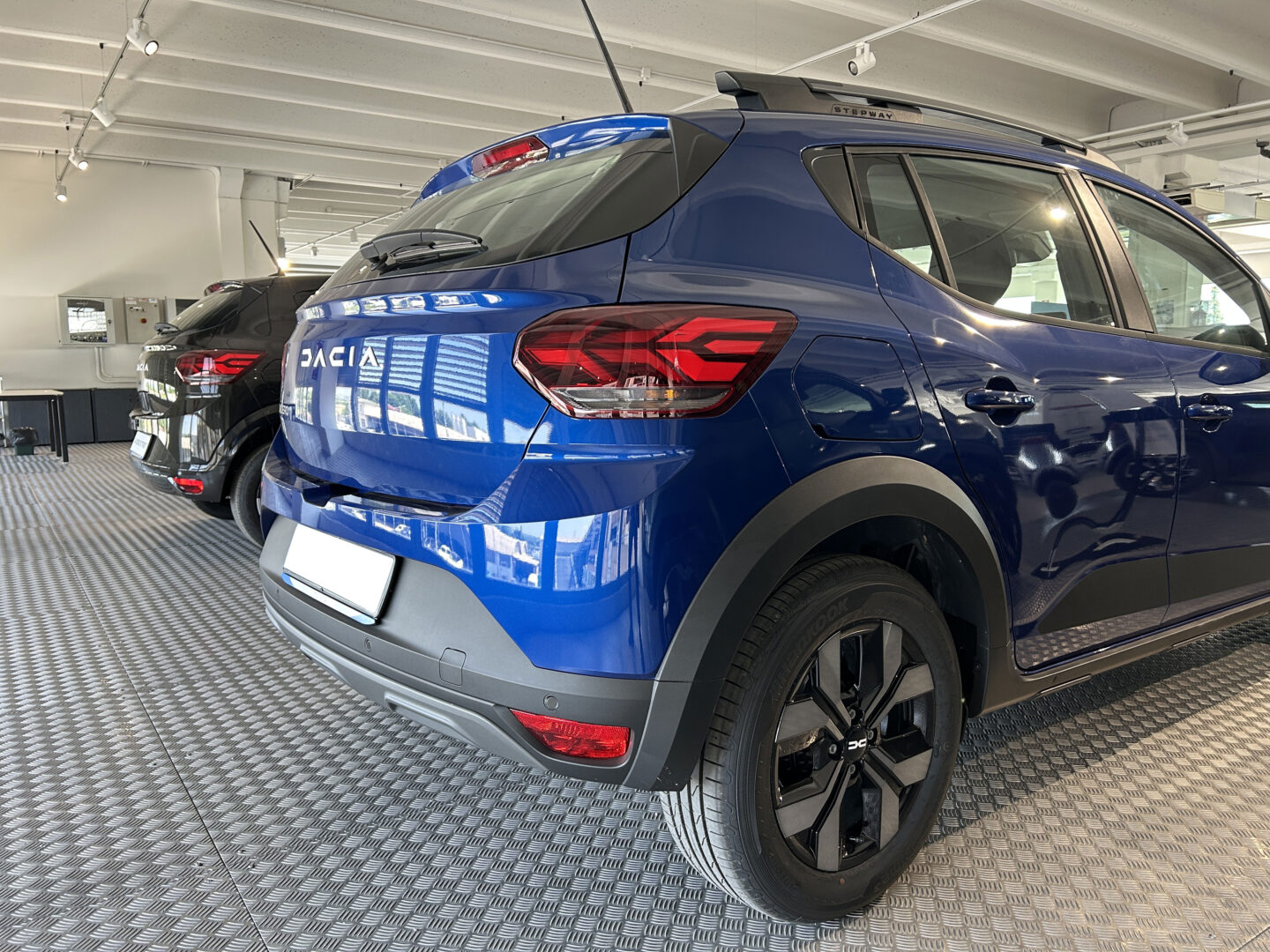 Vista posteriore laterale della Dacia Sandero Stepway blu in esposizione, con cerchi in lega neri, dettagli SUV e badge Stepway visibile sopra la portiera.