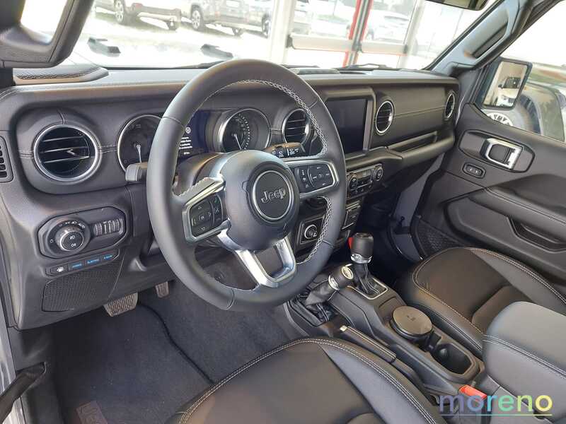  Interni di una Jeep Wrangler con volante multifunzione in pelle con logo Jeep, plancia con schermo centrale, comandi per climatizzazione e cambio.