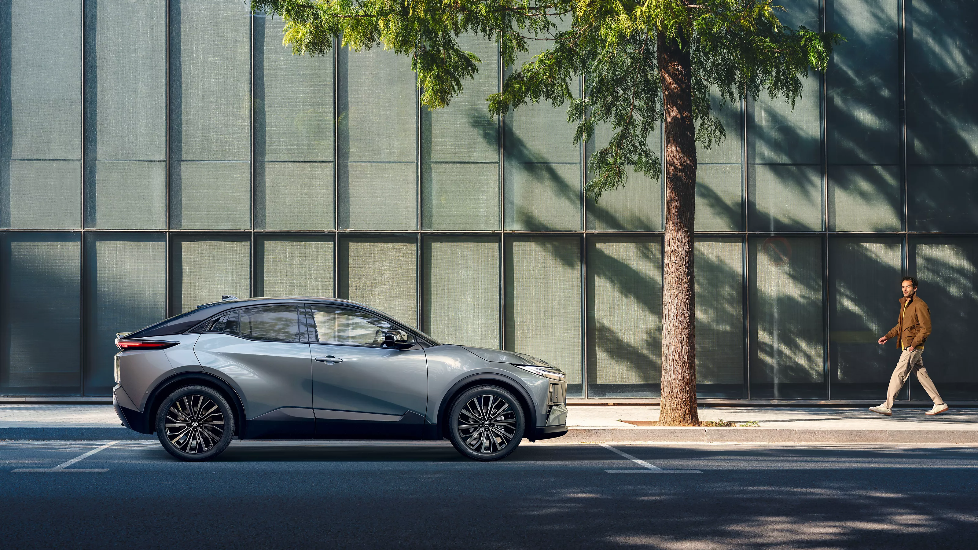 fiancata laterale della Toyota C-HR+ grigia su sfondo urbano 